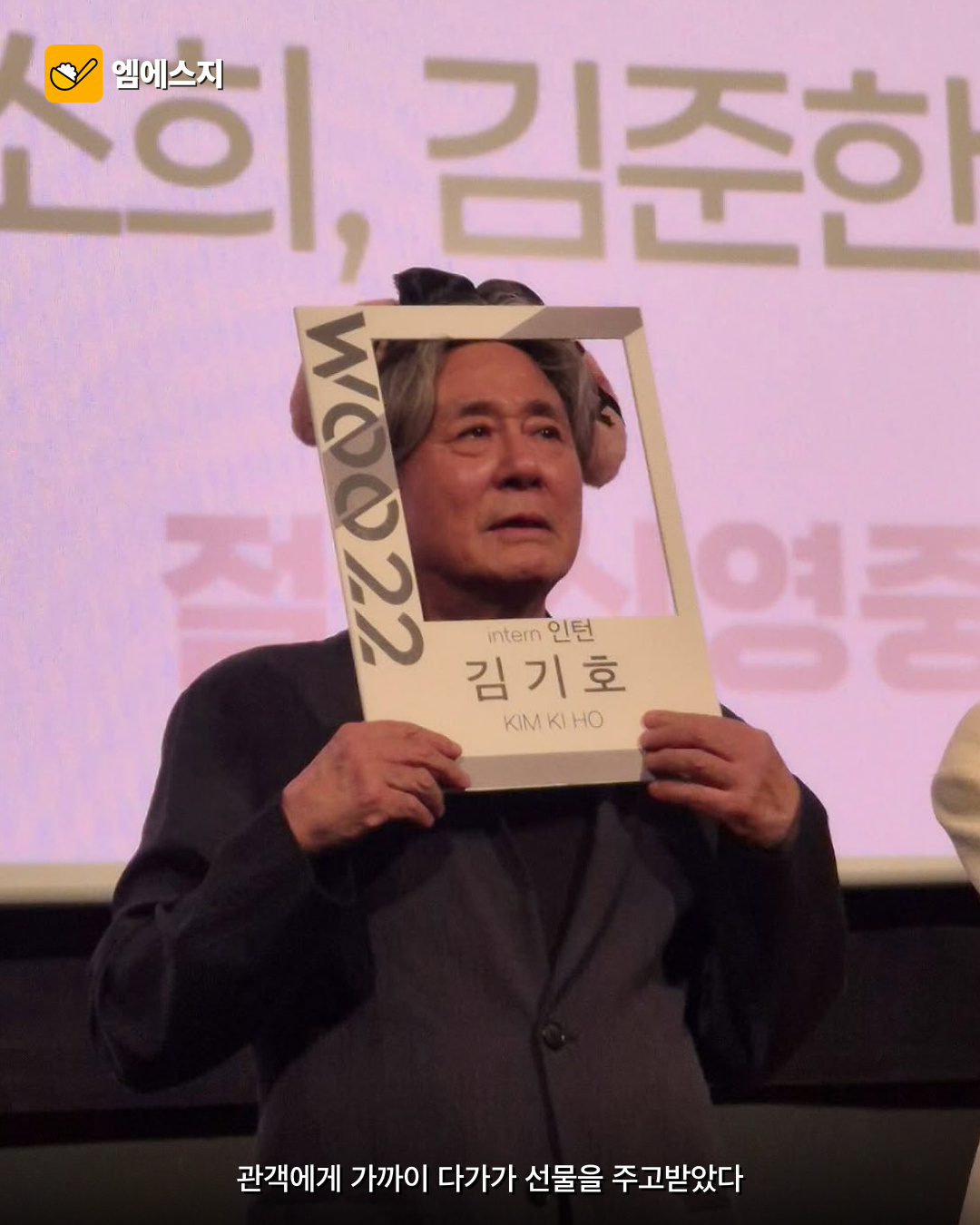 최민식이 팬이 건넨 영화 인턴 기호 캐릭터 액자를 든 장면